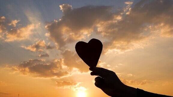 剪影的心形纸板在手和阳光透过心在日落的背景爱情和情人节