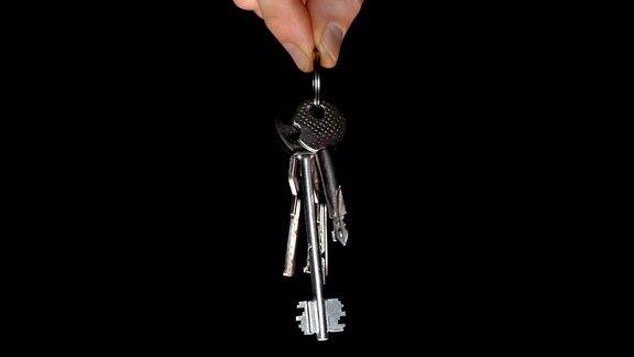 一串闪亮的镀铬公寓钥匙在一个男性的手在一个黑色的背景