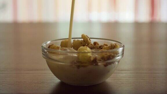 把酸奶和玉米片倒入一个透明的玻璃碗里放在家里的木桌上在阳光下烹饪