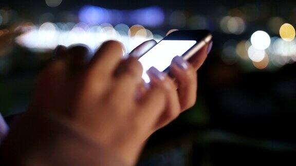女性用她的手机近处夜晚的城市灯光背景