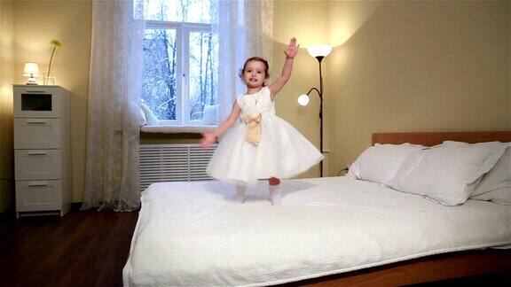 小烦躁不安穿着白色连衣裙的可爱小女孩在卧室的床上跳