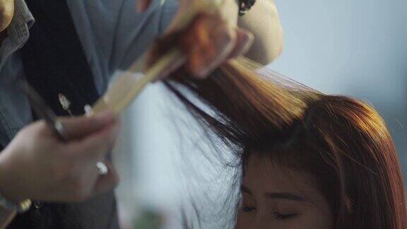 慢动作亚洲华人女性发型师梳理光滑的长发为她的客户在美发沙龙