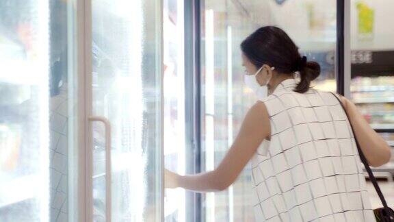 年轻的亚洲女性在超市的冷冻室里选择和挑选产品戴上防护灰尘和病毒的面罩保持健康