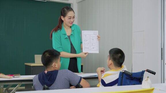 十几岁的亚洲男孩集中精力学习做一个英语作业美丽的老师解释在教室学校与一个残疾的朋友在轮椅上后视镜里的同学们正幸福地坐在桌旁