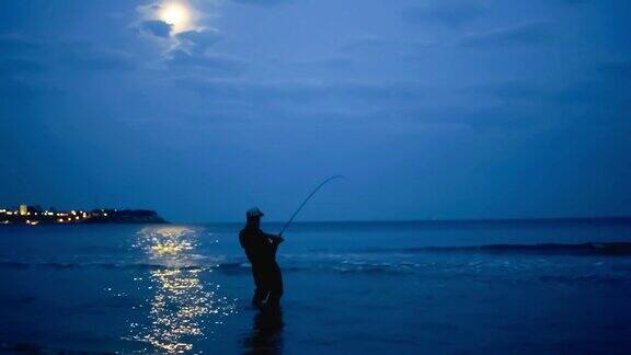 渔夫晚上在月亮的映衬下在海边钩住一条鱼