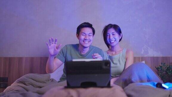 亚洲成人情侣结婚夫妇享受唱歌和幸福舞蹈一起移动手挥手看音乐会在线从笔记本或平板电脑在家里的床上居家隔离的生活方式