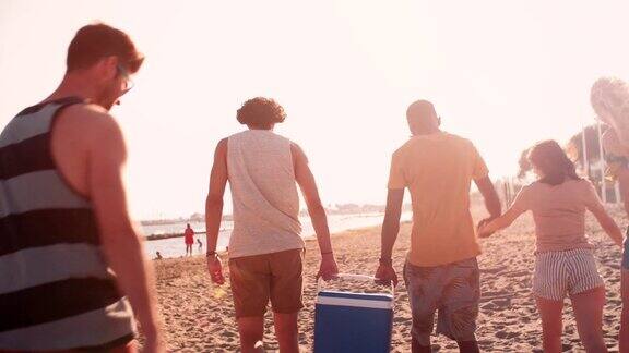 年轻的多民族朋友拿着冷却器在海滩上散步