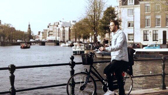 一个在河桥上骑着自行车的4K欧洲男人休闲时尚的男性类型在智能手机上看周围享受风景