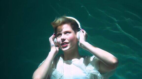 快乐美丽的年轻女子听着音乐戴着耳机眼睛闭在水下慢动作