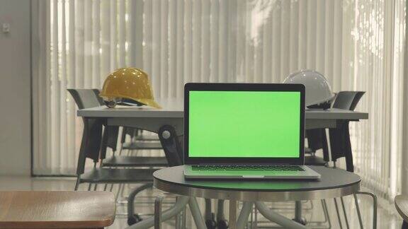 现场拍摄的笔记本电脑显示绿色色度键屏幕站在办公室与工程安全帽技术在背景技术背景