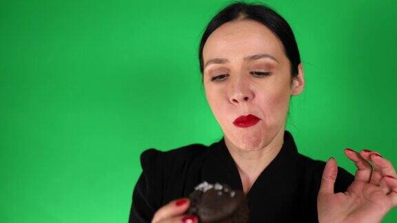 现代女性品尝巧克力松饼在绿色背景前愉快地做着鬼脸