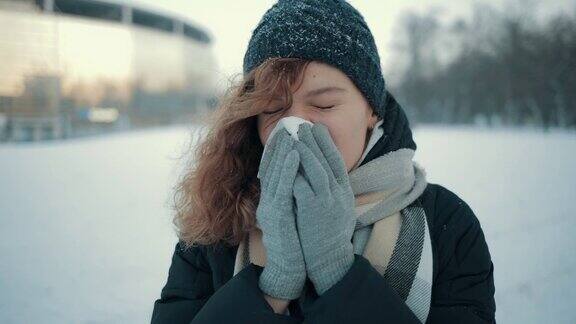 一个生病的年轻女子在下雪的冬天在户外用手绢擤鼻子