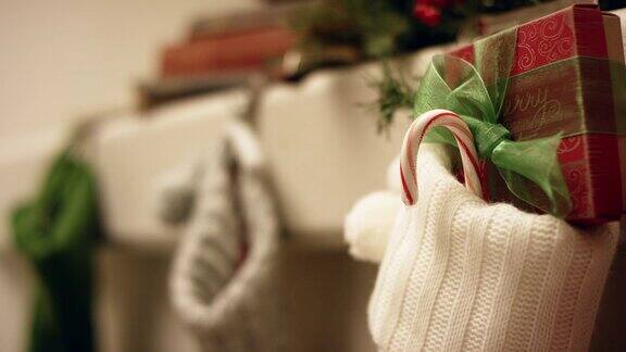 圣诞老人戴着手套的手把一个红白条纹拐杖糖放在圣诞长袜里挂在壁炉架上