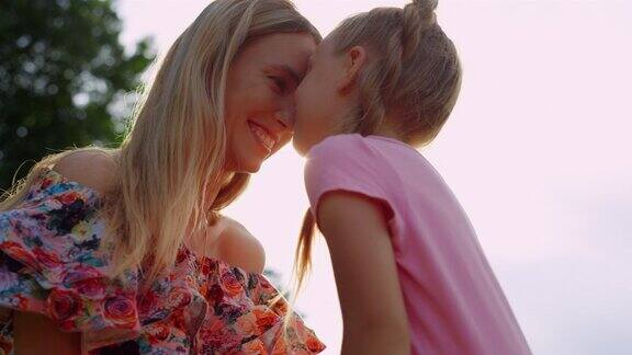 女儿在城市公园亲吻妈妈女人和女孩在户外欣赏日落
