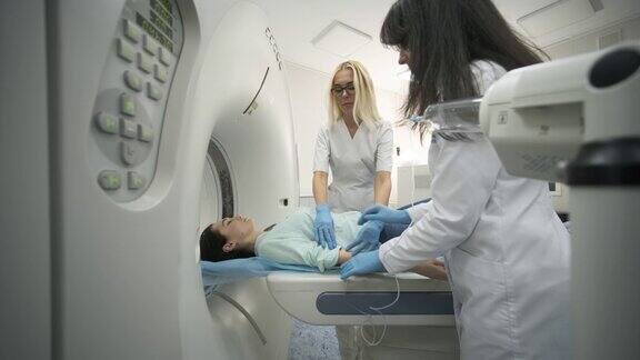 在现代医学诊所两名放射科医师插入静脉导管注射造影剂给正在接受CT或MRI扫描的女性患者病人躺在CT或MRI扫描床上在机器内移动