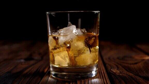 一杯加冰的威士忌在灯光下的黑暗木质背景上