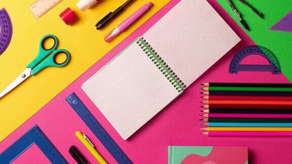 定格动画组成的多颜色的文具物品摆放在桌子上平铺粉红色、黄色、绿色背景复制空间笔记本4k镜头视频动态