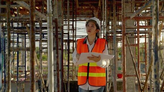 拿着图纸的年轻的亚洲女工程师正在施工现场走动检查施工是否按计划进行