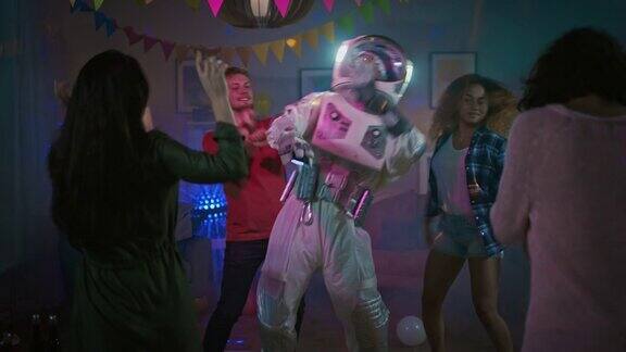 在大学宿舍的化妆舞会上:有趣的家伙穿着太空服跳舞做机器人现代舞和他在一起漂亮的女孩和男孩在霓虹灯下跳舞