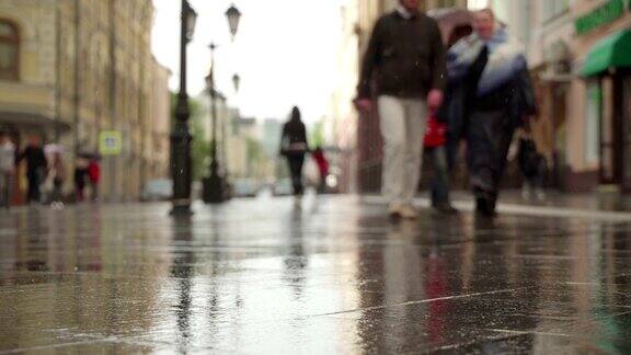 倒影剪影的人在水池湿沥青在雨背景雨天的城市街道真正的时间人们在雨中带着雨伞上下班模糊的散景自然背景