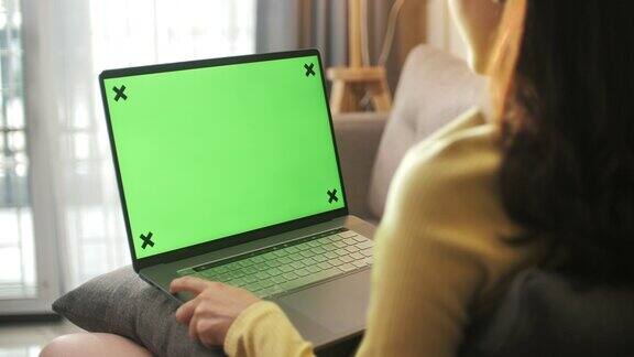 坐在沙发上看着绿色屏幕的笔记本电脑的女人