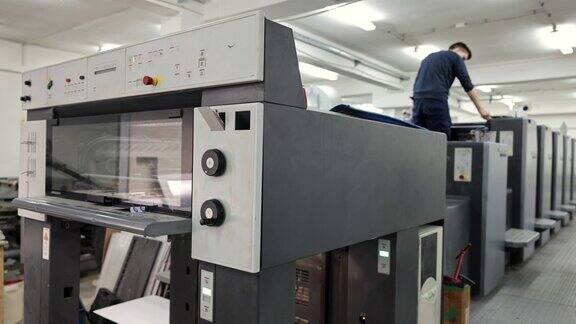 印刷厂有敬业的工人一边戴着防护口罩一边做着自动化印刷机的质量控制
