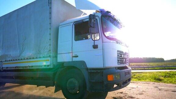 摄像机跟随卡车与货物拖车在公路上行驶和运输货物阳光明媚的日子里一辆卡车在乡间公路上疾驰阳光照在背景上慢镜头