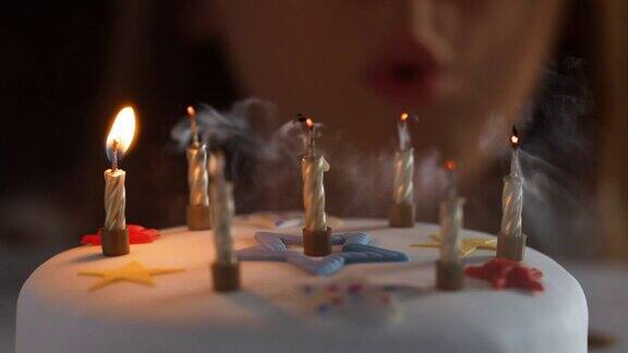 一个女人吹灭七个点燃的蜡烛在一个白色的装饰的生日蛋糕一个派对吹风机旁边散焦灯在背景细节