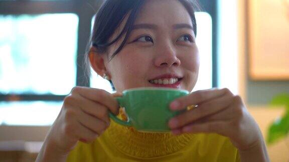 快乐的年轻亚洲女人在咖啡馆喝拿铁咖啡