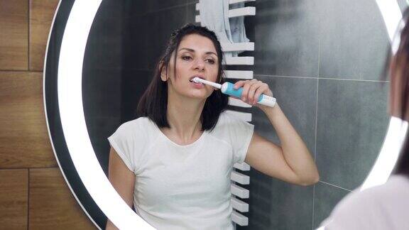 可爱自信的30岁黑发女人穿着白色t恤在浴室的镜子前刷牙