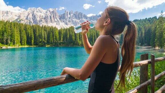 一个女人在山上的湖边放松用一个可重复使用的水瓶喝水