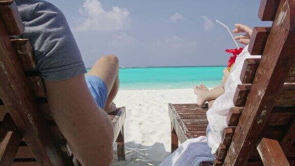 在马尔代夫阳光明媚的热带海滩上一对夫妇在躺椅上畅饮椰子饮料