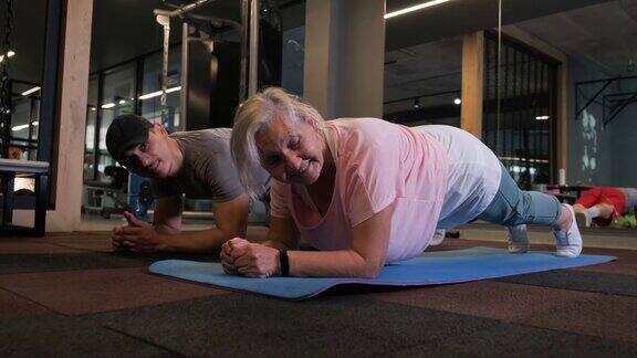 年轻的私人教练协助他的老年病人在瑜伽垫上练习平板支撑