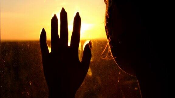 窗外的剪影女人在夕阳下把手放在玻璃上慢动作