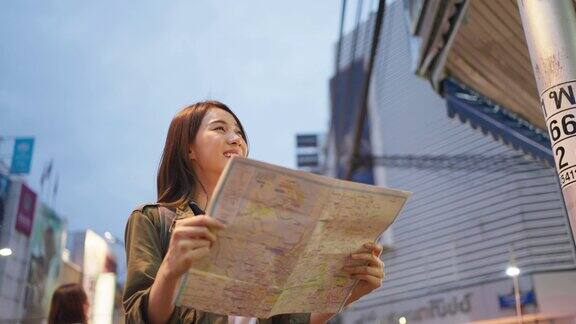 亚洲年轻女背包客在地图上寻找目的地迷人美丽的旅游女孩独自在街上旅行享受步行在城市的夜晚在泰国度假旅行