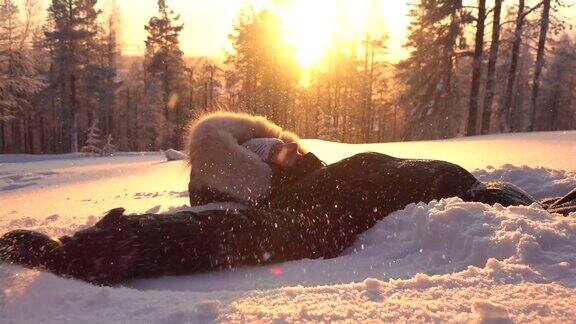 慢动作顽皮的女孩在金色的夕阳下在新鲜的雪中制造雪天使