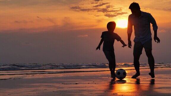 一对父子在黄昏的沙滩下快乐的踢球