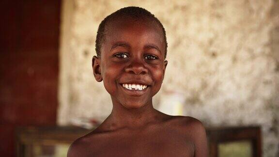 一个顽皮的真实的非洲孩子的特写肖像看着相机和微笑的强烈模糊的背景快乐活力的黑人男孩与世界分享他美丽的笑容