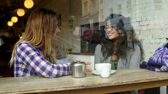 快乐的女性朋友坐在咖啡馆里喝着咖啡聊天