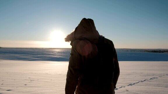 一个穿着夹克背着背包的男人在冬日的夕阳下踏上田野