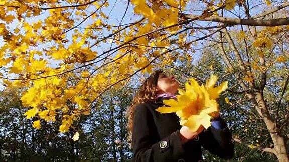 在秋天的公园里一个女孩从树枝上扔下黄叶