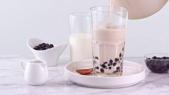 将奶茶倒入玻璃杯中配以台湾流行的木薯珍珠泡放在明亮的大理石桌上和白色托盘上这是自制4k视频拍摄