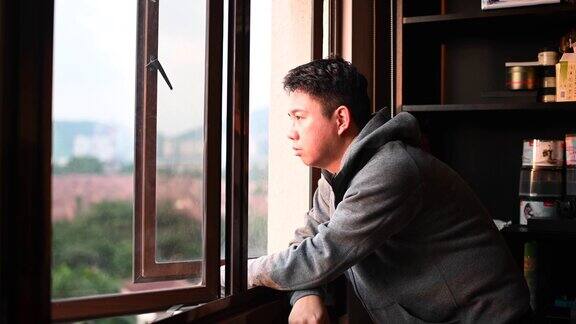 日落时分一名身穿连帽衫的亚洲华人中年男子从家中望向窗外表情严肃