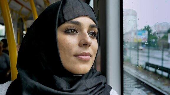 年轻甜美的穆斯林妇女戴着头巾在公共汽车的雨窗里看着交通概念城市概念天气概念梦想概念
