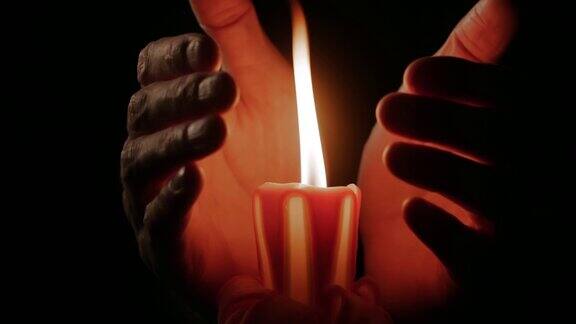 手被点燃的蜡烛温暖着黑暗中在燃烧着火焰的蜡烛周围举起手来