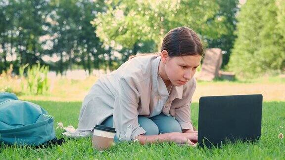 一名女学生坐在户外使用她的笔记本电脑学习