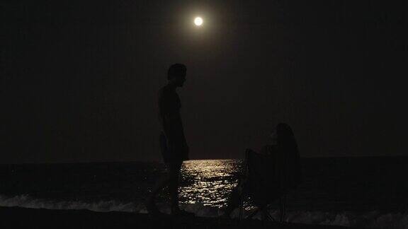 女孩坐在海边的椅子上看月亮男人走过去吻了她