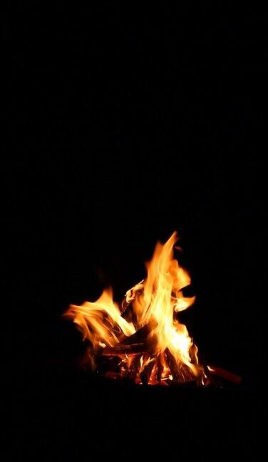 大篝火与砍过的木头在一个黑色的背景特写火焰孤立自然背景与小火花垂直视频