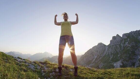 慢镜头:快乐的年轻女子在山顶上跳跃并伸出双臂