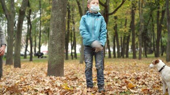 无忧无虑的男孩戴着冠状病毒口罩在秋天的公园里扔黄叶两个积极的高加索兄弟有乐趣休息狗户外关于Covid-19大流行的休闲